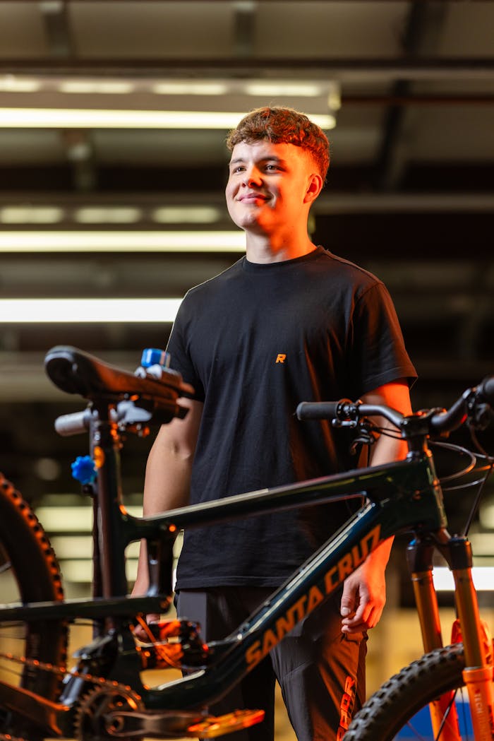 why-choose-us Teen smiling while standing beside a Santa Cruz bicycle indoors, showcasing contentment and satisfaction.